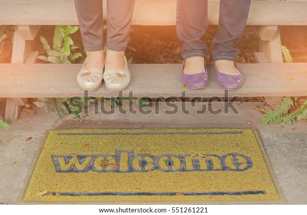 shoes of two woman on stair and welcome carpet blur\
is under stair