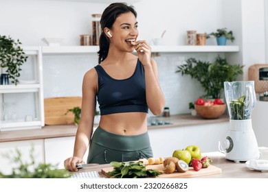 Shoot of athletic woman cutting fruits and vegetables to prepare a smoothie while listening to music with earphones in the kitchen at home - Powered by Shutterstock