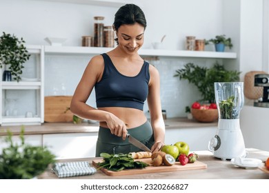 Shoot of athletic woman cutting fruits and vegetables to prepare a smoothie while listening to music with earphones in the kitchen at home - Powered by Shutterstock
