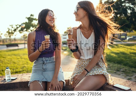 Shoot of two beautiful young women eating ice cream while having fun walking through the park in the city.