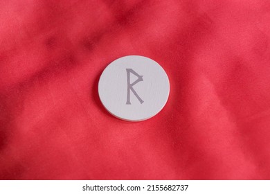 shooting of a circle of white wood on a red background with a rune engraved, in particular it is the letter Raido