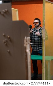 Shooting range instructor in protective gear demonstrates how to load a magazine into a pistol for tactical training in an indoor facility.
