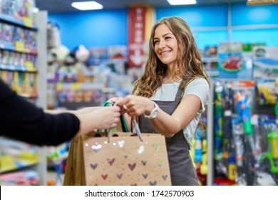 Shop Assistant Give Shopping Bags To A Female Customer. Attractive Woman Shop Keeper Giving Paper Bag To Buyer.