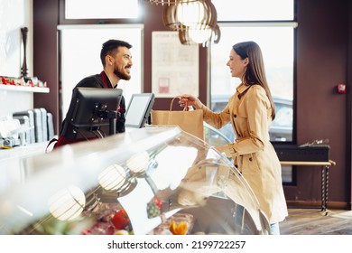 Shop assistant handling shopping bag to female customer in grocery store - Powered by Shutterstock