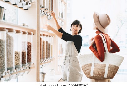 Shop Assistant Helping Customer In Bulk Food Store. Seller Advising Woman In Her Purchase Of Groceries Without Plastic Packaging In Zero Waste Shop. Sustainable Shopping At Small Local Businesses.