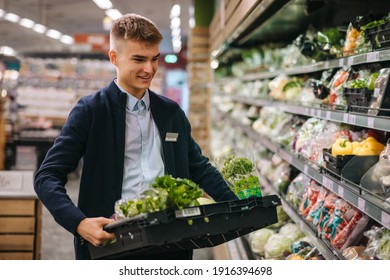 Shop assistant in supermarket re-stocking fresh vegetables in shelves of produce section. - Powered by Shutterstock