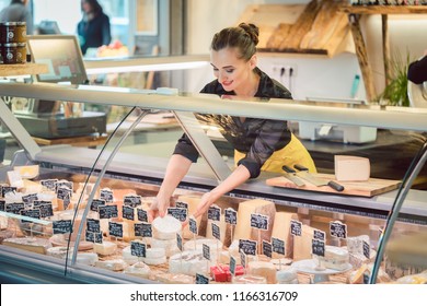 Shop clerk woman sorting cheese in the supermarket display to sell it - Shutterstock ID 1166316709