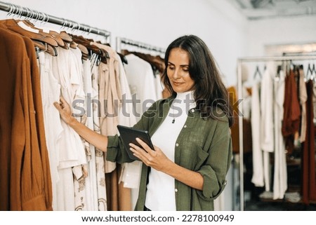 Shop owner conducting a quality control check in her clothing boutique using her digital tablet. Business woman carefully inspecting each garment to ensure that her customers receive the best items.