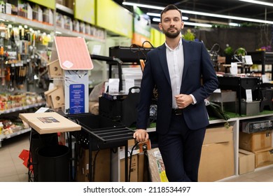 Shop Owner Next To A Rack Of Picnic Supplies, Barbecue Grills And Barbecue Grills In A Hardware Store