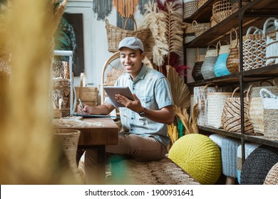 The shop owner notes with a pen while using a digital tablet while sitting in a craft store - Shutterstock ID 1900931641