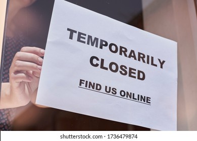 Shop Or Restaurant Worker Hanging A Paper With Warning - Temporarily Closed. Find Us Online. Closed Because Of Coronavirus Or Covid-19 Pandemic