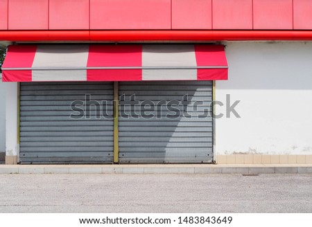 Shop retail with metal shutters closed and a red white awning. Sidewalk and asphalt road in front. Urban background for copy space