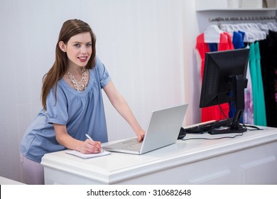 Shop Worker Using Laptop By The Till In Fashion Boutique