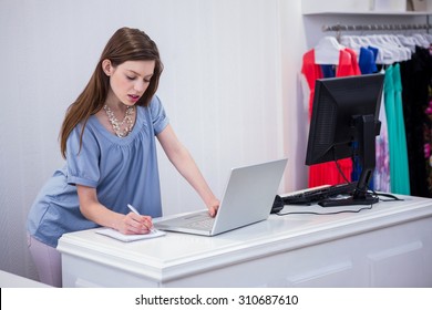 Shop Worker Using Laptop By The Till In Fashion Boutique