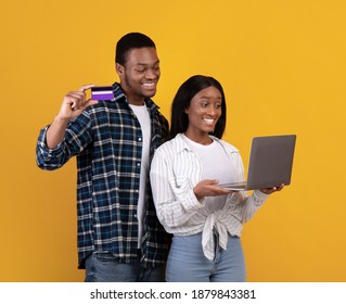 Shopaholics, Online Shopping And Emotions Of Success. Smiling Millennial African American Students Husband And Wife Paying Bill On Laptop And Showing Credit Card, Isolated On Yellow Background