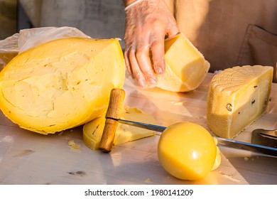 Shopkeeper's Hands Cutting A Head Of Cheese Close Up. Artisan Cheese In A Street Market. Cheese Maker Cutting Cheese In His Workshop. Food Festival In The City Park. Street Fast Food.