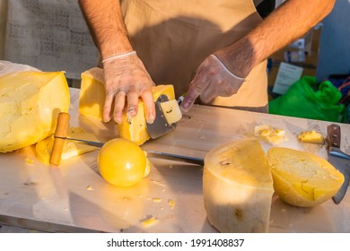 Shopkeeper's Hands Cutting A Head Of Cheese Close Up. Artisan Cheese In A Street Market. Cheese Maker Cutting Cheese In His Workshop. Food Festival In The City Park. Street Fast Food.