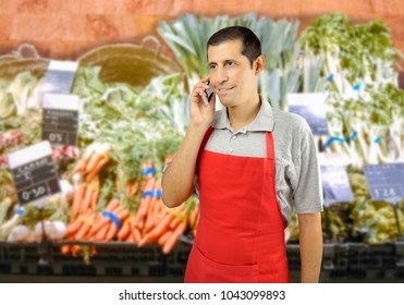 Shopman With Apron Using A Smart Phone At The Greengrocer