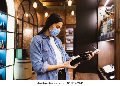 Shopper In Liquor Store During Covid-19 Outbreak, Young Woman Wearing Face Mask To Protect Against Virus Holding Bottle Of Wine.