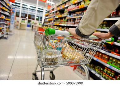 A Shopper Pushes A Trolley Along A Supermarket Aisle - Image Has A Shallow Depth Of Field