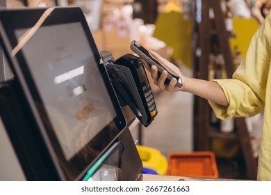 Shopper using smartphone to make a contactless payment at a supermarket checkout, utilizing NFC technology for a quick and convenient transaction