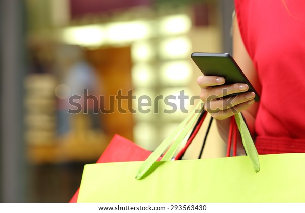 Shopper woman hand shopping with a smart phone and\
carrying bags