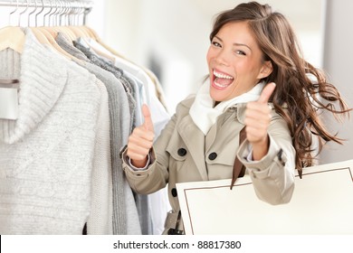 Shopper Woman Happy Shopping And Buying Clothes. Joyful Excited Smiling Woman. Mixed Race Caucasian / Chinese Asian Female Model Holding Shopping Bags In Coat Inside In Clothing Store Giving Thumbs Up