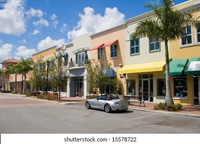 A shopping area with condos above stores that is designed to mimic a turn of the century, small town Main Street -- with  modern sport's car parked at curb.