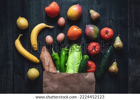 Shopping bag full of vegetables, fruits, eggs and bread on wooden background. Dark food photography. Rising prices of basic foodstuffs