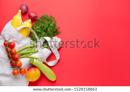 Shopping bag with many healthy vegetables and fruits on color background
