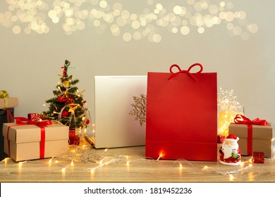 Shopping bag with mockup and laptop among gift boxes on wooden table with blurred lights background. Christmas shopping online concept. - Powered by Shutterstock