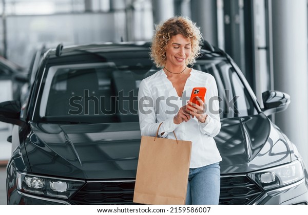 With shopping bag. Woman with curly blonde\
hair is in autosalon.