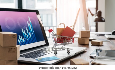 Shopping bags in shopping cart and credit card on laptop with paper boxes  and sales data economic growth graph on screen, buying and selling services online on network, online shopping and e-commerce