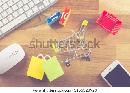 Shopping bags, supermarket cart, grocery basket, smart phone, keyboard and mouse computer on wooden background. Worldwide online shopping b2c e-commerce on internet website or social media at home.