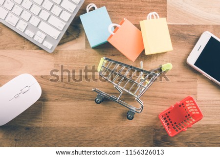 Shopping bags, supermarket cart, grocery basket, smart phone, keyboard and mouse computer on wooden background. Worldwide online shopping b2c e-commerce on internet website or social media at home.