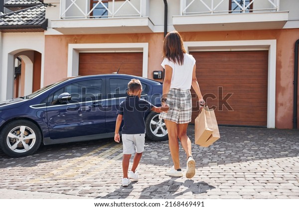 With shopping bags. Woman with little boy\
near the the modern automobile at\
daytime.