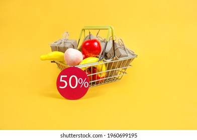 a shopping basket with fruit and gift boxes on a yellow background and a red sign that says 50 percent off