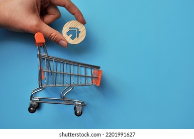 A Shopping Basket And A Wooden House Above It. Symbol Of Buying And Selling Housing