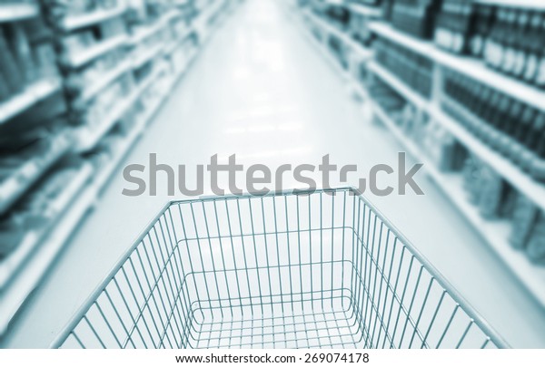 shopping cart and blurred supermarket background. \
Closeup detail of a consumer woman shopping in a supermarket ,\
retail business shop.