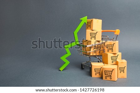 Shopping cart with cardboard boxes with a pattern of trading carts and a green up arrow. Increase the pace of sales, production of goods. Improving consumer sentiment. Strategy for increasing revenue