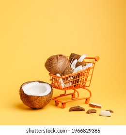 Shopping cart with coconuts against vibrant orange background. Creative food delivery service concept. Summer tropical exotic fruit banner with copy space. Vegetarian diet banner idea.