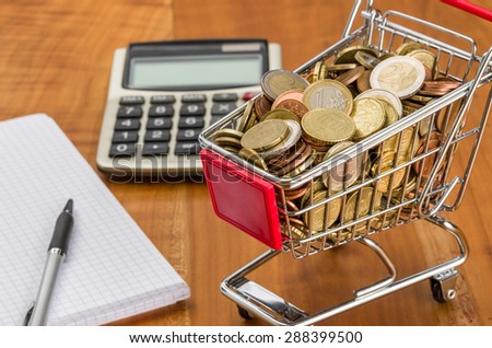 Shopping cart filled with coins on a wooden desk