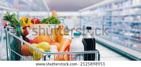 Shopping cart filled with food and drinks and supermarket shelves in the background, grocery shopping concept
