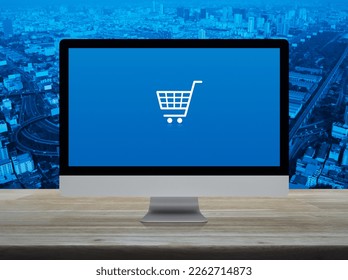 Shopping cart flat icon on desktop modern computer monitor screen on wooden table over city tower, street, expressway and skyscraper, Business shop online concept