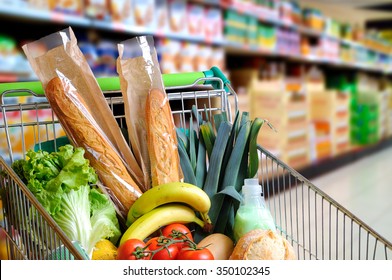 Shopping cart full of food in the supermarket aisle. High internal view. Horizontal composition
