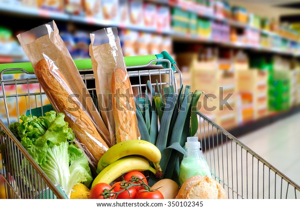 Shopping cart full of food in the\
supermarket aisle. High internal view. Horizontal\
composition