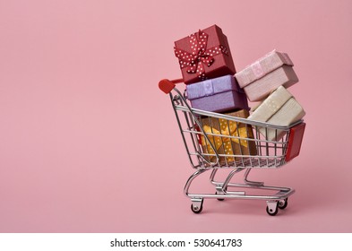 a shopping cart full of gifts of different colors on a pink background, with a negative space