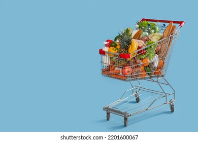 Shopping cart full of groceries on light blue background. Space for text