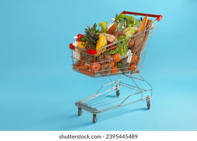 Shopping cart full of groceries on light blue background - Shutterstock ID 2395445489