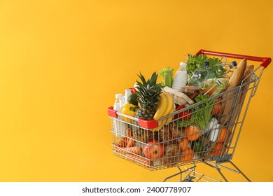 Shopping cart full of groceries on yellow background. Space for text